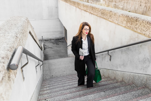 Business woman with newspaper and bag walking up stairs 