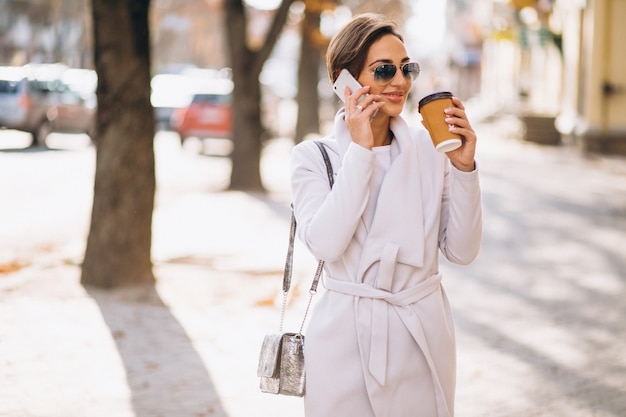 Business woman with phone drinking coffee outside in street