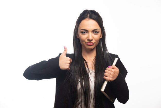 Business woman with thumb up holding clipboard on white wall