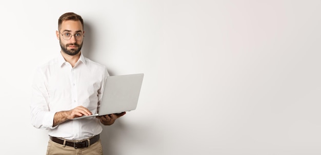 Free photo business young handsome businessman working on laptop doing job on computer standing over white back