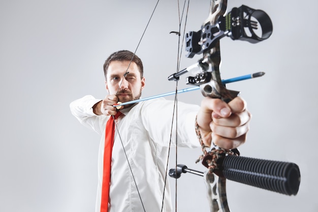 Free Photo businessman aiming at target with bow and arrow, isolated on gray studio background. the business, goal, challenge, competition, achievement concept