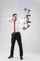 Free photo businessman aiming at target with bow and arrow, isolated on gray studio background. the business, goal, challenge, competition, achievement concept