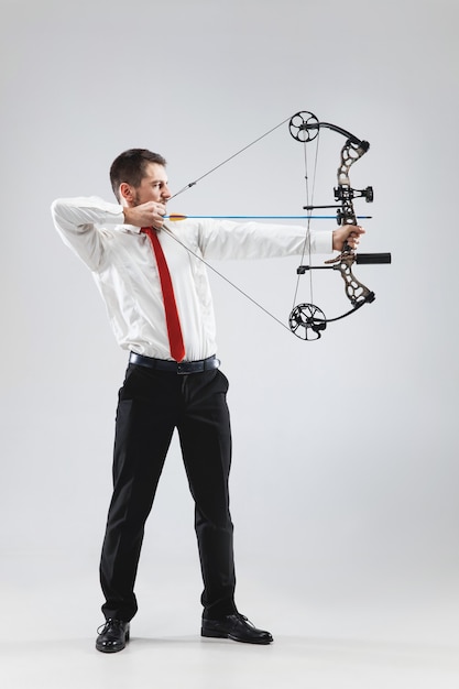 Free photo businessman aiming at target with bow and arrow, isolated on gray studio background. the business, goal, challenge, competition, achievement concept