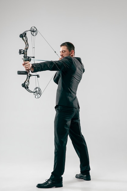 Free photo businessman aiming at target with bow and arrow, isolated on gray studio background.