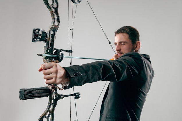 Free photo businessman aiming at target with bow and arrow isolated on gray studio background.