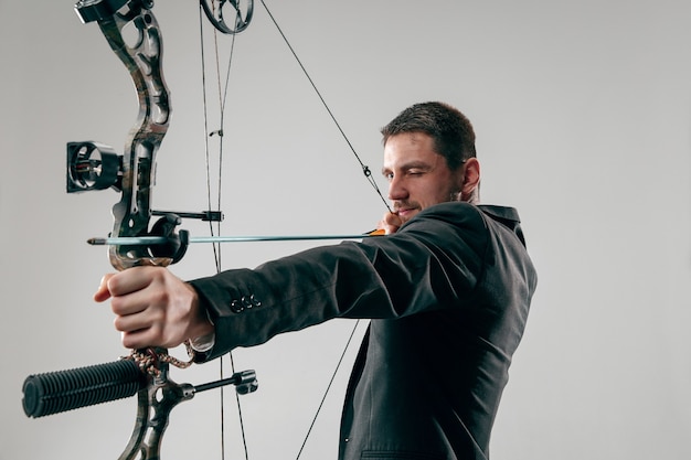 Businessman aiming at target with bow and arrow isolated on gray studio wall