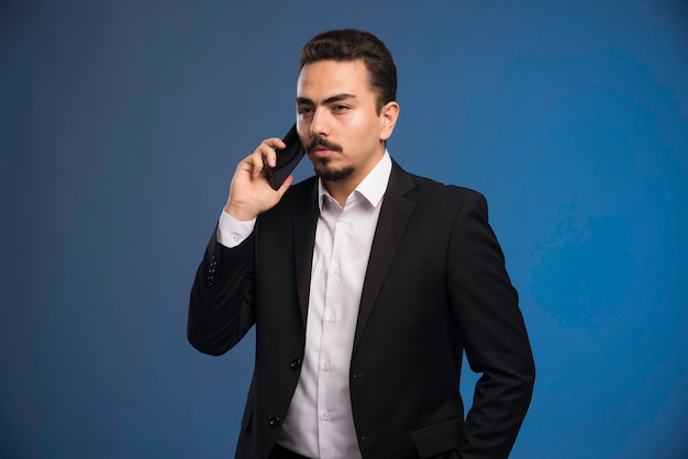 Businessman in black suit talking to the phone. 