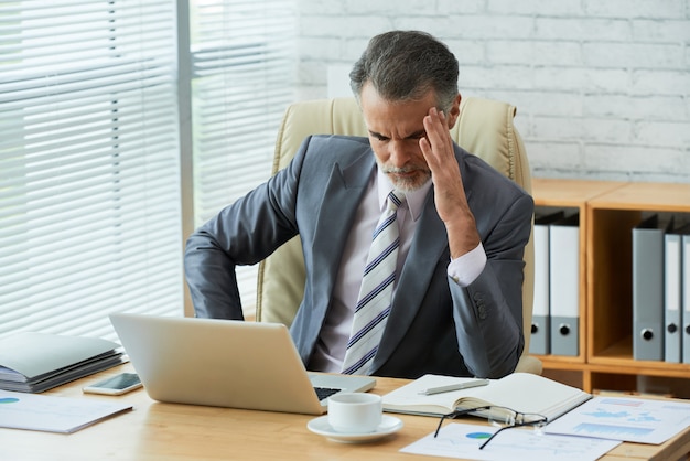 Businessman concentrated on computer data touching his head in headache