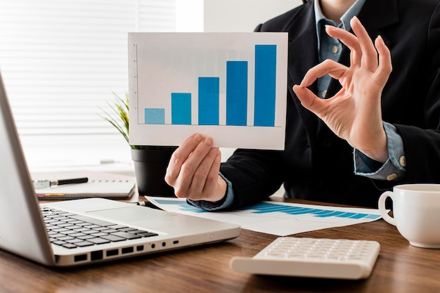 Free photo businessman doing the ok sign while holding growth chart