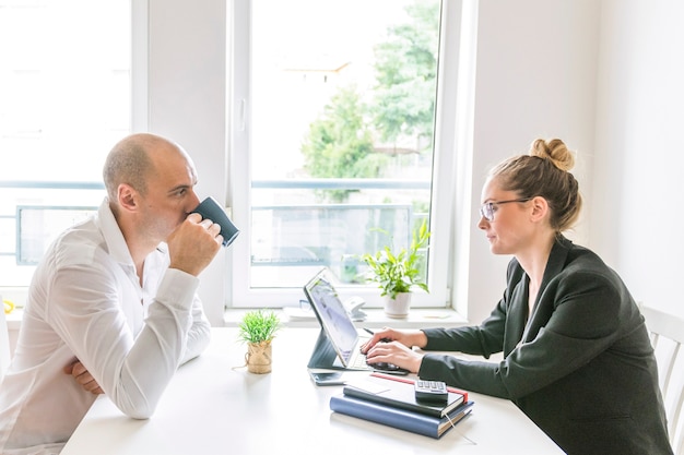 Businessman drinking coffee looking at his partner working on laptop