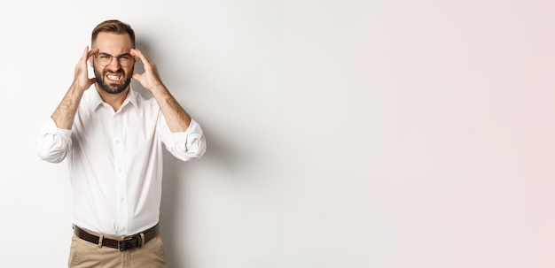 Businessman having headache grimacing and holding hands on head standing over white background