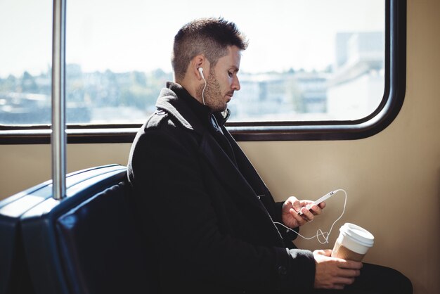 Businessman holding a disposable coffee cup and listening to music on mobile phone