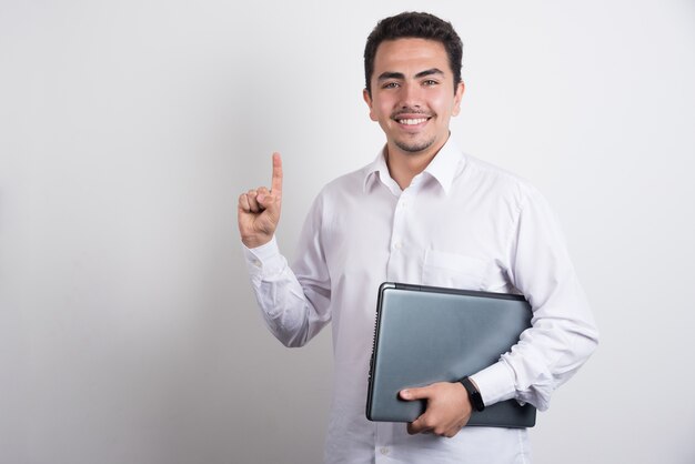 Businessman holding laptop and pointing up on white background.