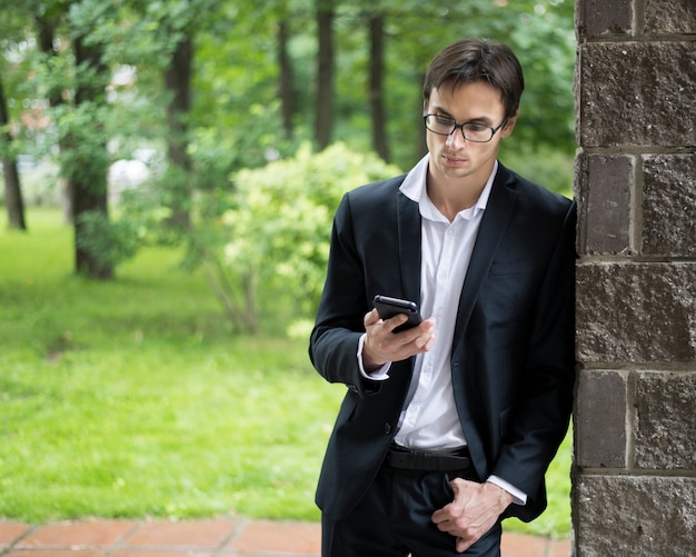 Businessman leaning on wall and checking phone