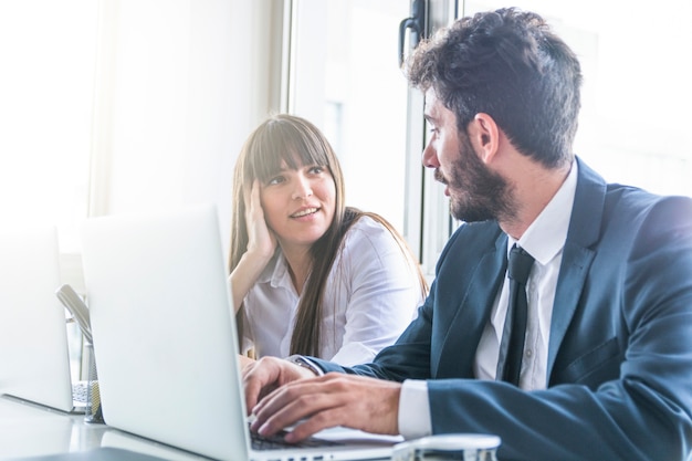 Free photo businessman looking at smiling young woman using laptop