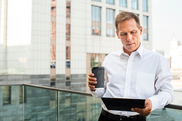 Free photo businessman looking at tablet while holding coffee