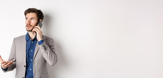 Free photo businessman making phone call talking on smartphone and looking busy wearing suit white background