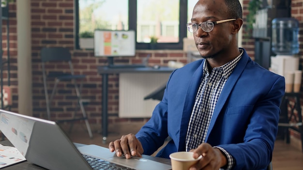 Businessman planning financial strategy in brick wall office, working on startup job. Project manager using statistics to find information for business project on web browser. Handheld shot.