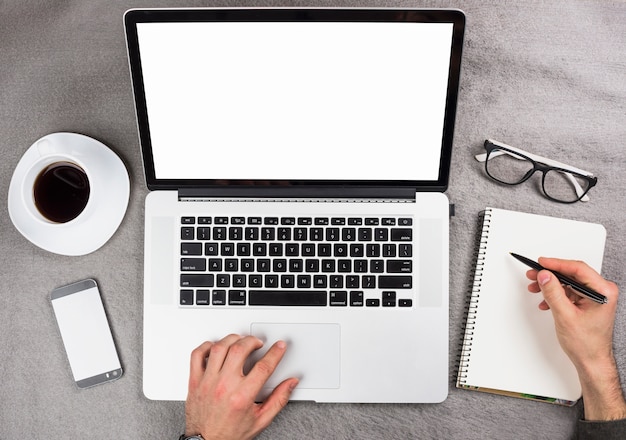 A businessman's hand using digital tablet writing on spiral notepad over the gray desk