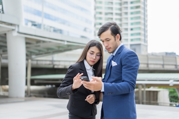 Businessman showing mobile phone to colleague outside.