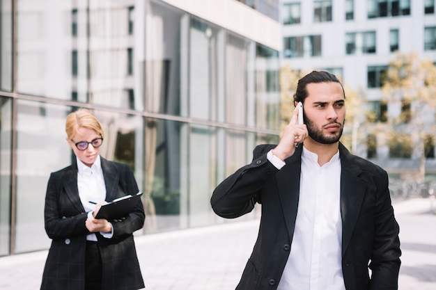 Businessman standing in front of busy businesswoman talking on cell phone