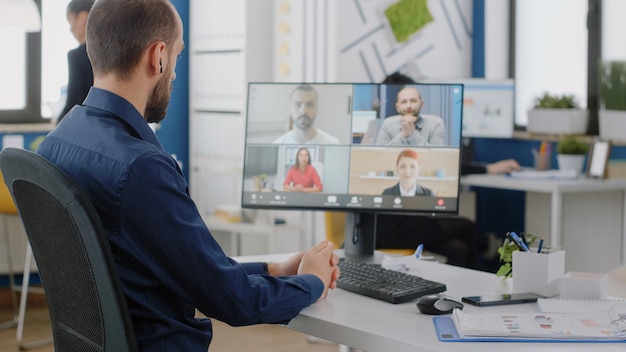 Free photo businessman talking to team of colleagues on video call for project briefing at office. engineer using online conference on computer for meeting about business strategy and development