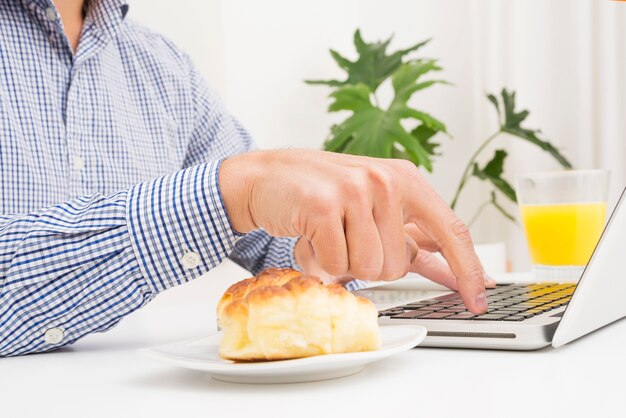 Businessman typing on laptop with bread and glass of juice on table