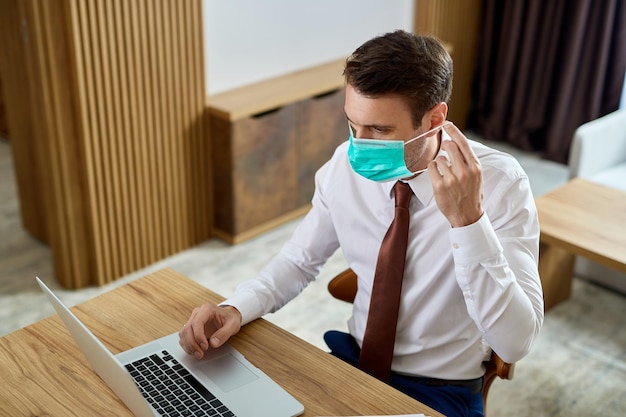 Free Photo businessman using laptop and putting on protective face mask while working in a hotel room