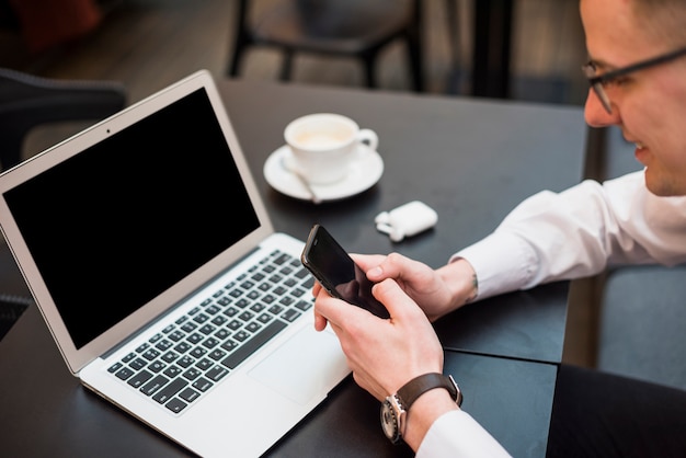 A businessman using the mobile phone in front of laptop with coffee cup on table