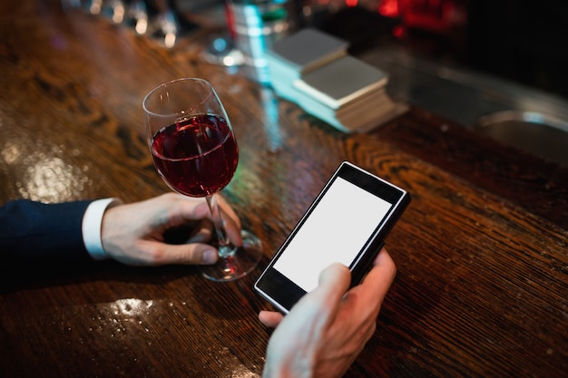 Businessman using mobile phone with glass of red wine in hand