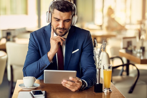 Free photo businessman wearing headphones while surfing the net on touchpad in a cafe