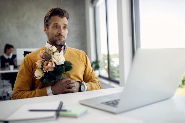 Free photo businessman with bouquet of flowers making video call over laptop in the office