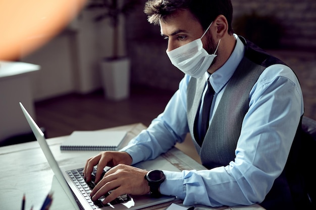 Businessman with face mask working on laptop in the office during coronavirus pandemic