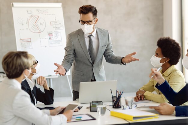 Businessman with protective face mask talking to coworkers on a meeting in the office