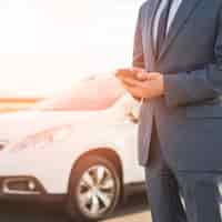 Free photo businessman with smartphone in front of car