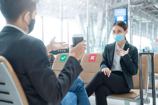 Businessman and woman with face mask protection casual meeting with social distancing seat at airport terminal new lifestyle business concept