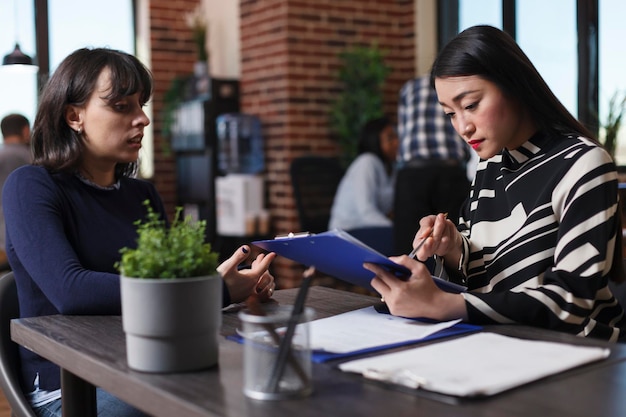 Businesswoman analyzing applicant cv resume asking recruitment question during interview meeting in startup company office. Asian manager recruiting woman for human resources job