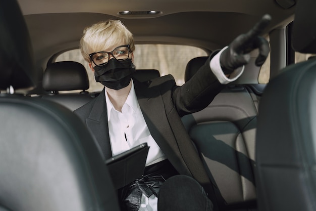 Free photo businesswoman in a black mask sitting inside a car