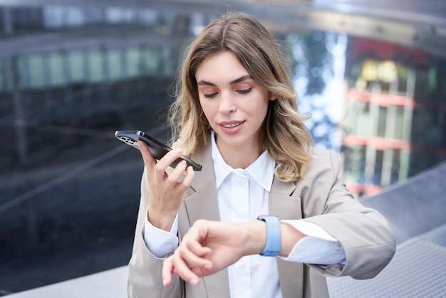 Businesswoman checks time on digital watch and records voice message arranges a meeting sits outside