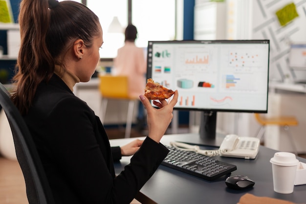 Free photo businesswoman enjoying food meal order in company office during takeout lunchtime break working at financial graphs