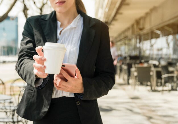 Businesswoman handing takeaway coffee cup standing in the outdoor restaurant