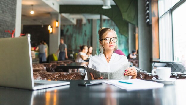 Businesswoman holding newspaper sitting in restaurant