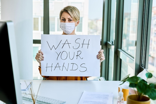 Businesswoman holding placard with wash your hands text as appeal during virus epidemic