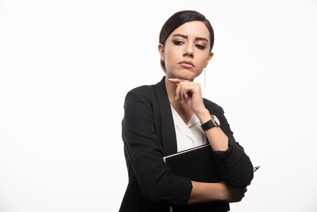 Businesswoman posing with notebook on white wall.