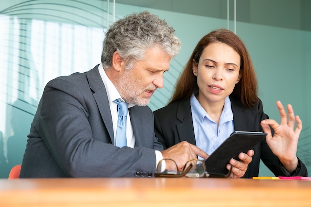 Businesswoman presenting project to investor. Serious female employee showing content on tablet to colleague, explaining details.