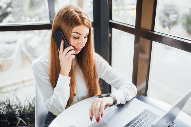 Businesswoman speaks on the phone and looks into the watch at the cafe