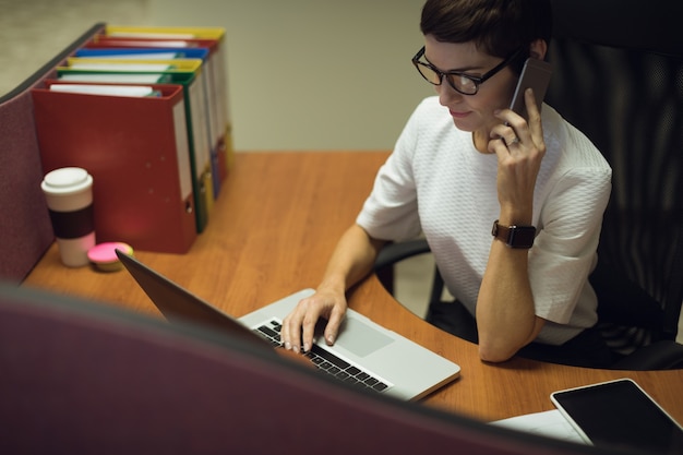 Free Photo businesswoman talking on mobile phone while using laptop in office