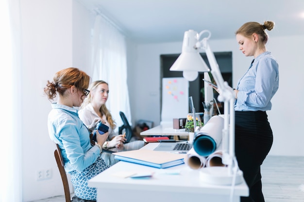 Free photo businesswoman using digital tablet standing near her colleague sitting in office