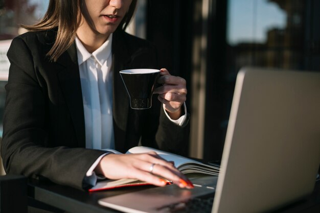 Businesswoman using laptop while having cup of coffee