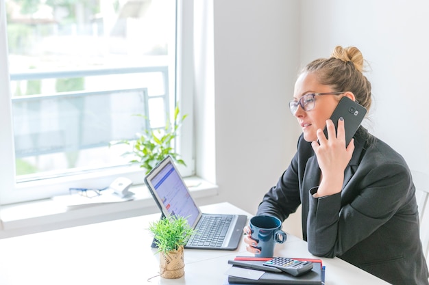 Businesswoman with cup of coffee talking on cellphone in office